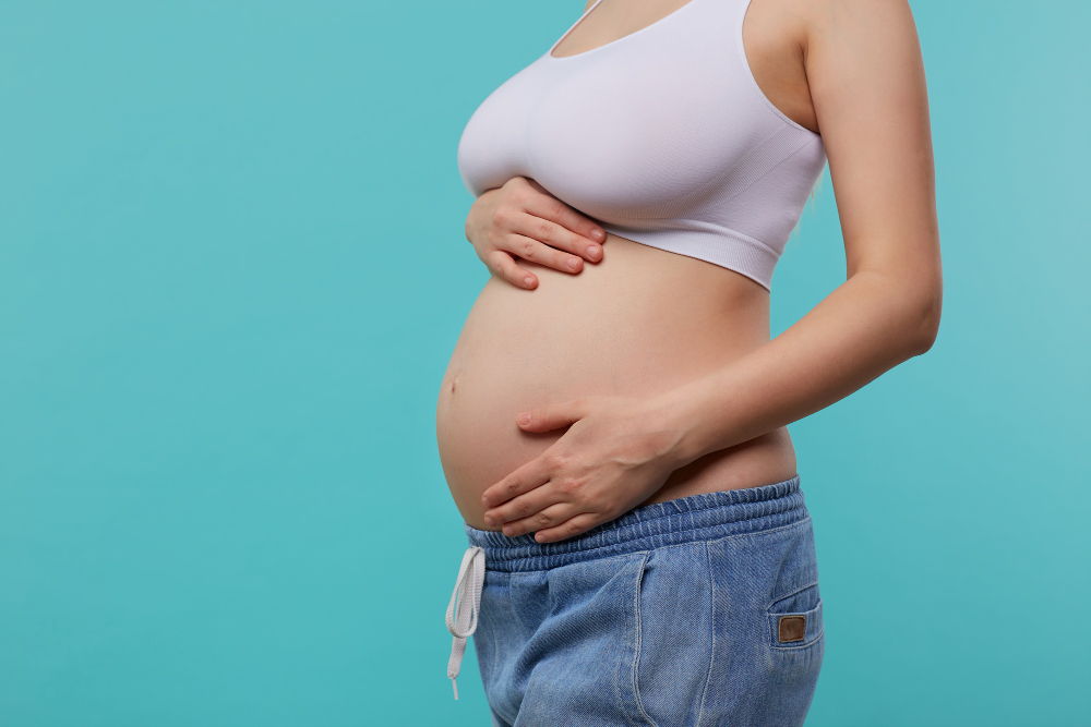 cropped photo young pregnant female dressed white sporty top jeans holding raised hands her belly while posing blue background
